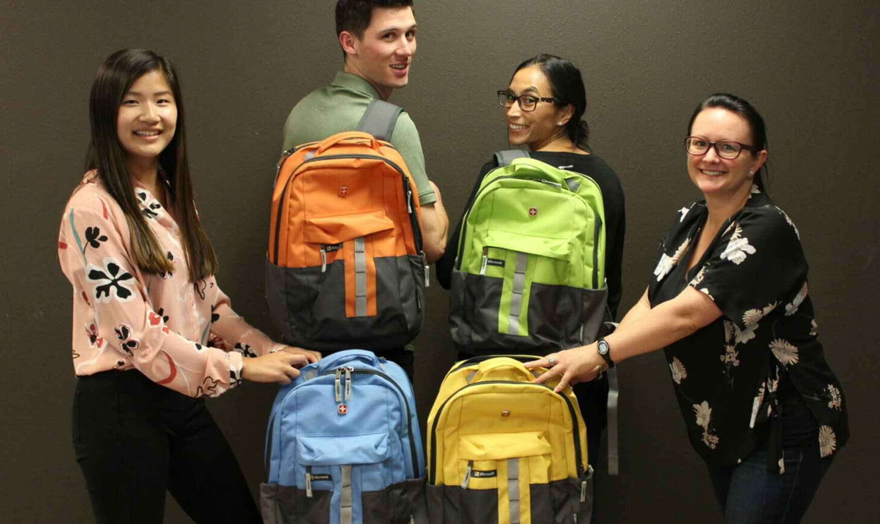 Image of four people holding custom colored backpacks in orange, green, blue and yellow.
