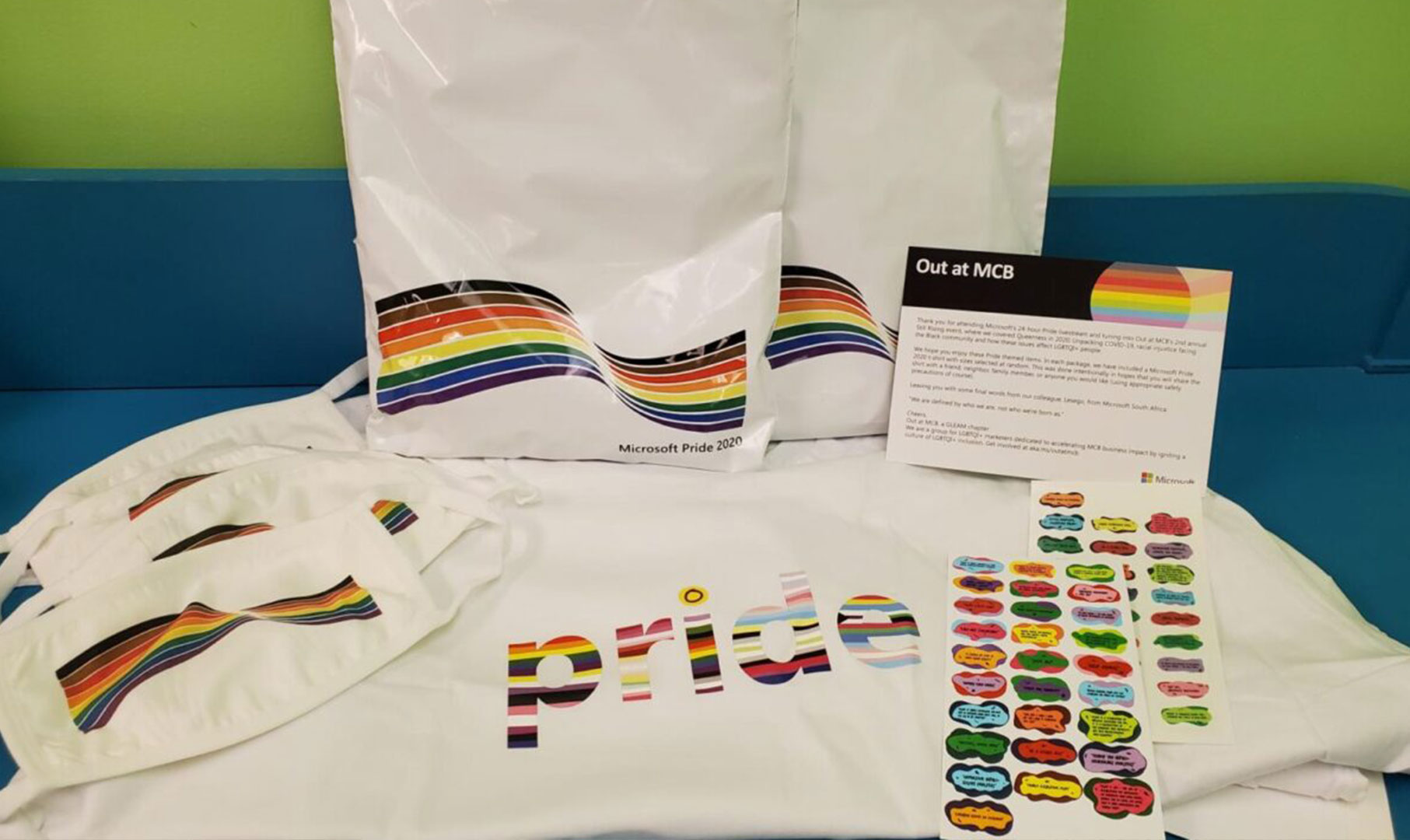 Image of sweatshirt with mulitcolor PRIDE word on it with a sheet of stickers and a set of two white face masks with the pride rainbow on them.