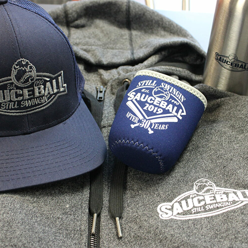 Image of baseball hat, can koozie and hooded sweatshirt laying on a table.