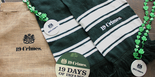 Image of various items with the 19 Crimes logo on them. Items include a green and white scarf, jute drawstring bag, necklace with green clovers and a coaster.