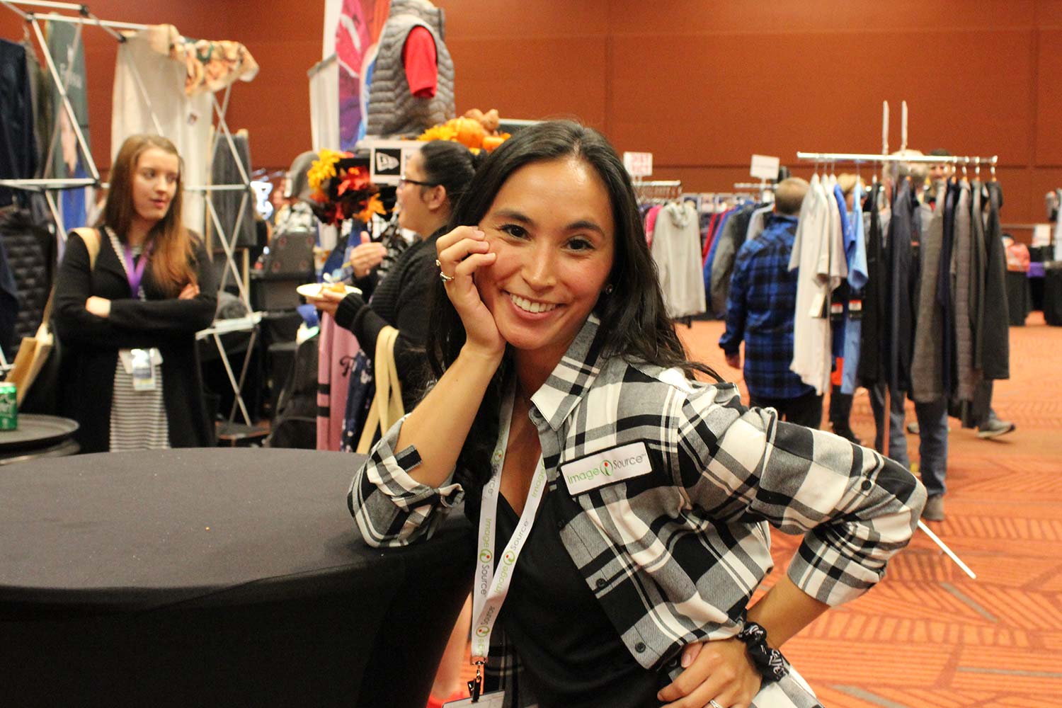 Image of women leaning on table at a tradeshow with apparel racks in the background.