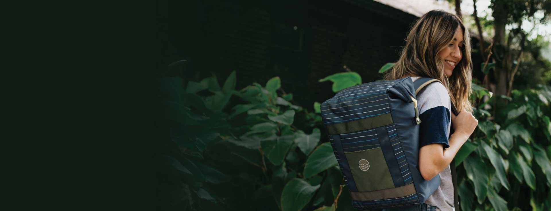 women wearing blue backpack walking by green bushes.