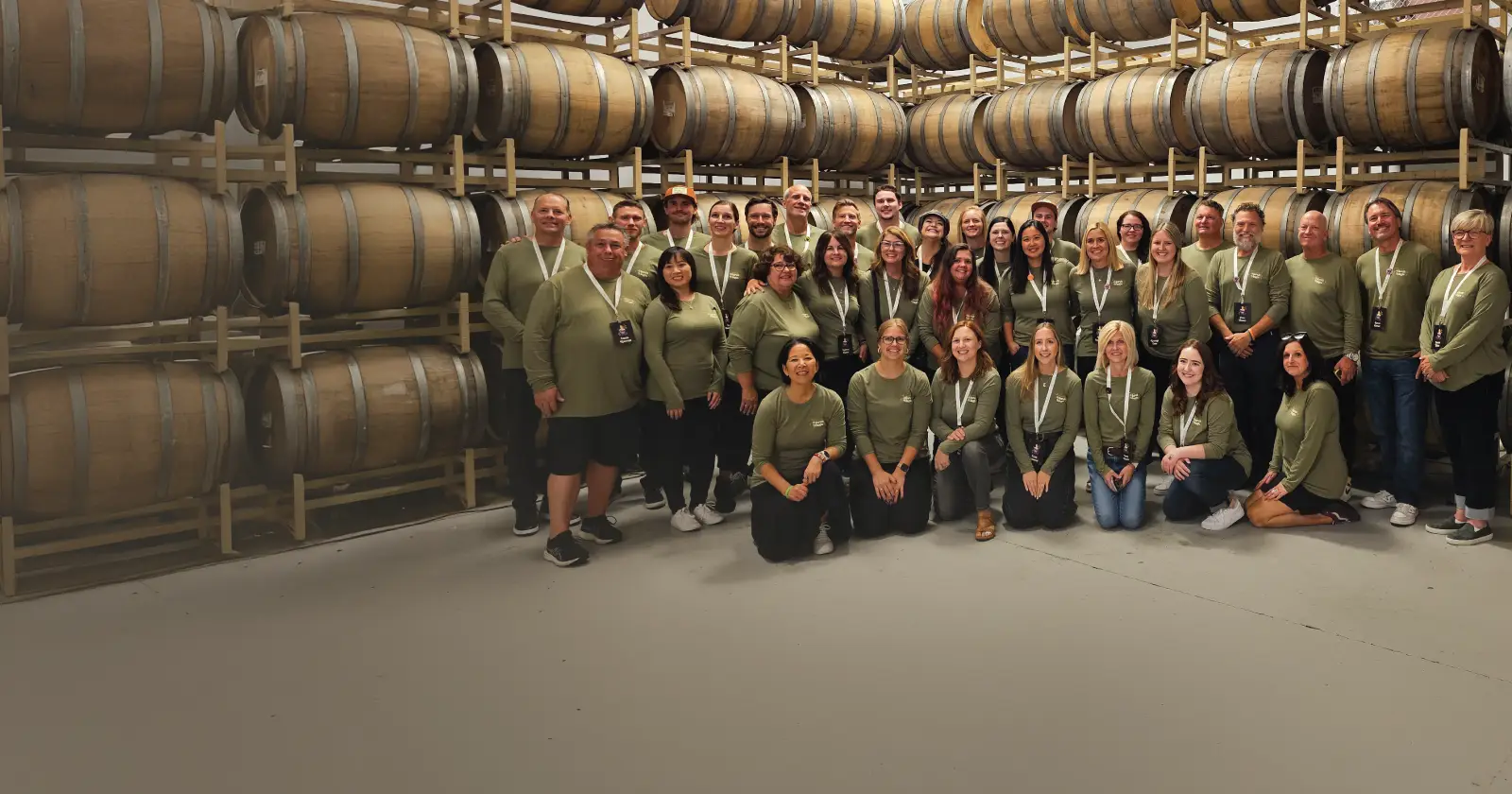 Group of people posing for picture in front of wine barrels.