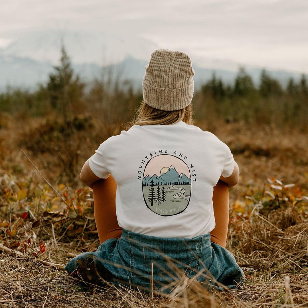 WA Woman sitting in field wearing a white t-shirt and beanie.