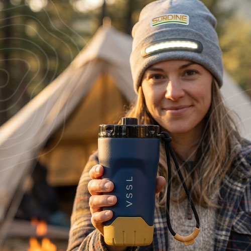 Lifestyle_Square Woman wearing beanie holding coffee tumbler at campsite.